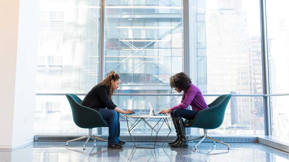 Zwei Frauen mit Laptops sitzen sich gegenüber